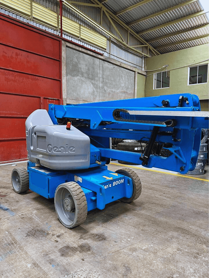 Blue Genie boom lift parked in an industrial warehouse with red and beige walls visible.