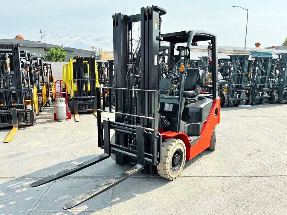 Red forklift parked among a row of other forklifts in an outdoor lot on a sunny day.